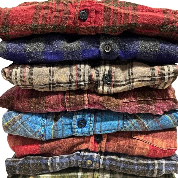Stack of folded acid-washed flannel shirts in red, blue and green plaid.